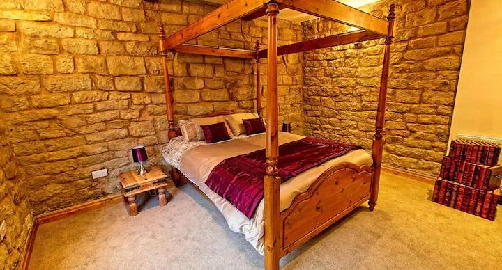 Wooden four post bed in bedroom with stone walls ready for guests