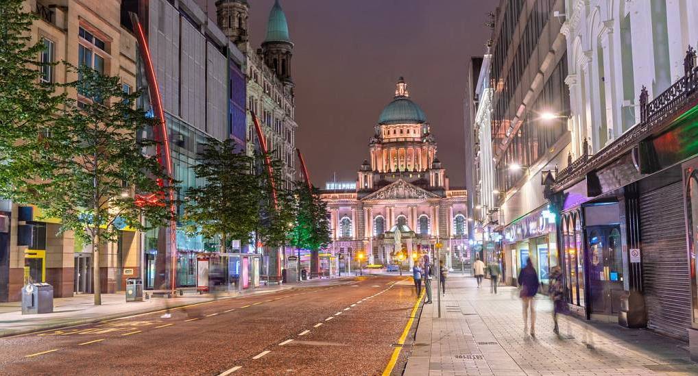 Illuminated Belfast City Hall and central city street at night, setting the stage for an epic Belfast stag do.
