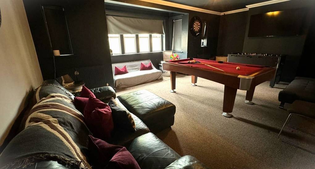 Spacious games lounge with red cloth pool table, foosball and dark walls at Upper Deck Fifty, Cardiff hen apartment.