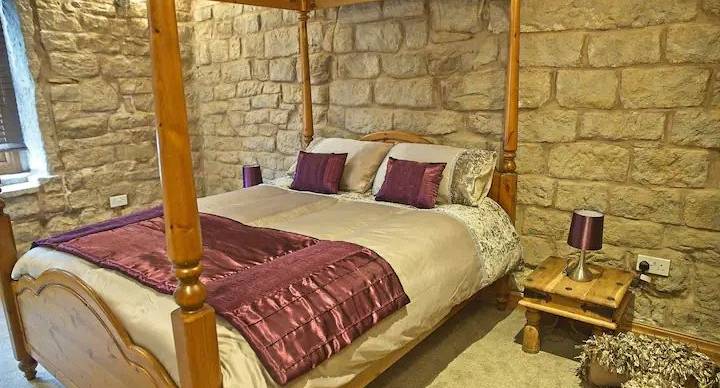 Four post bed with plum coloured throw and stone walls for that rustic and medieval feel