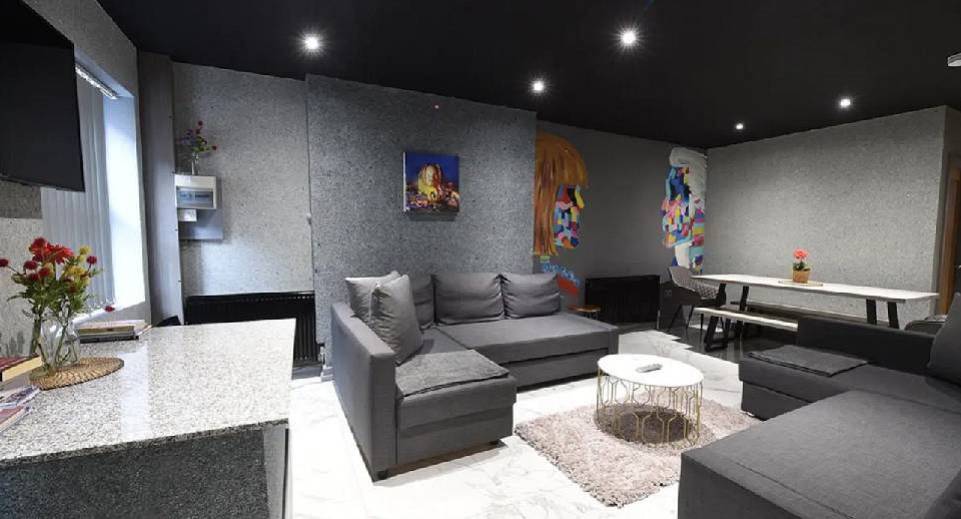 Contemporary lounge with grey corner sofa, art mural and long dining table at Overdrive townhouse Manchester.