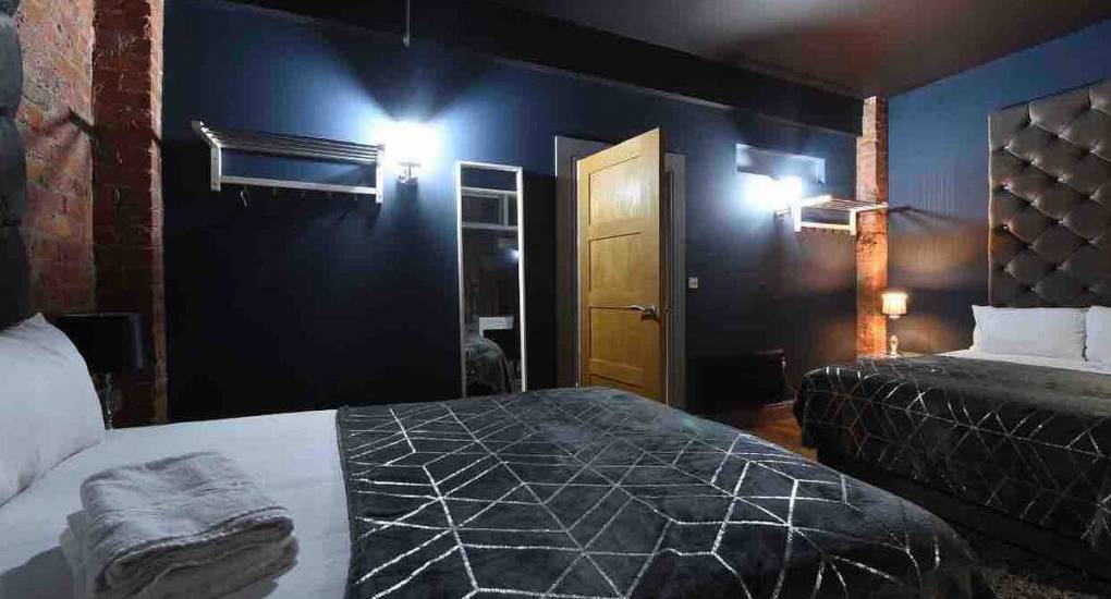 Spacious bedroom in the White House, Manchester party house showing two double beds with exposed brick walls in a rustic style