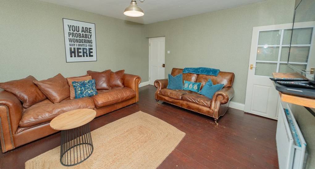 Spacious social seating in the lounge of Tranquil Escape near Newcastle, showcasing the rustic-modern decor, original wood flooring, and comfortable leather couches perfect for hen group relaxation.