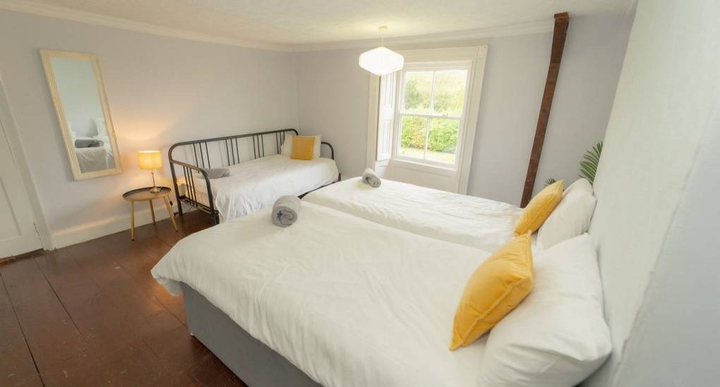 A cozy triple bedroom setup at Tranquil Escape featuring three single beds with vibrant yellow accents and views of the private estate grounds.